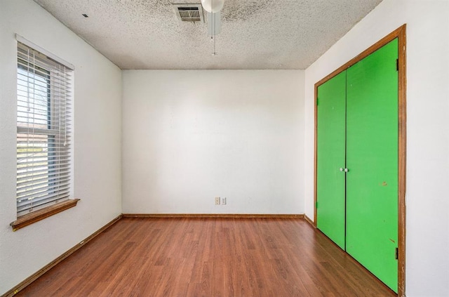 unfurnished bedroom featuring visible vents, a textured ceiling, wood finished floors, a closet, and baseboards