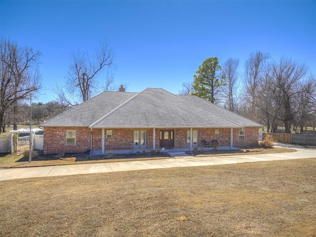 view of front of home featuring a front lawn, a porch, fence, brick siding, and a chimney