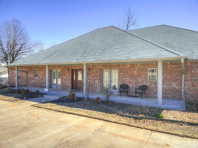 exterior space featuring brick siding, french doors, a porch, and roof with shingles