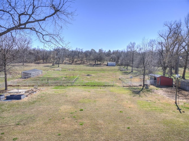 view of yard featuring a rural view, an outdoor structure, and fence