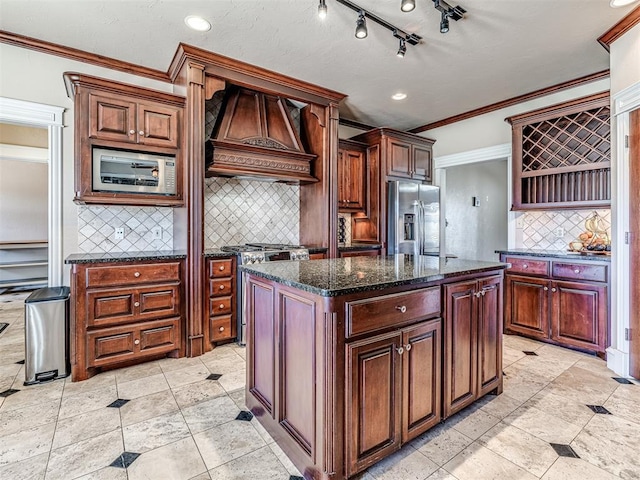 kitchen featuring dark stone countertops, premium range hood, ornamental molding, stainless steel appliances, and a center island