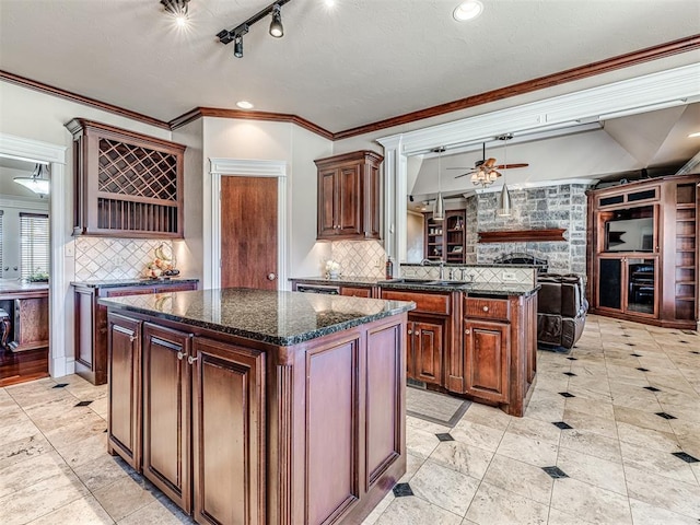 kitchen featuring a ceiling fan, a kitchen island, dark stone counters, a sink, and open floor plan