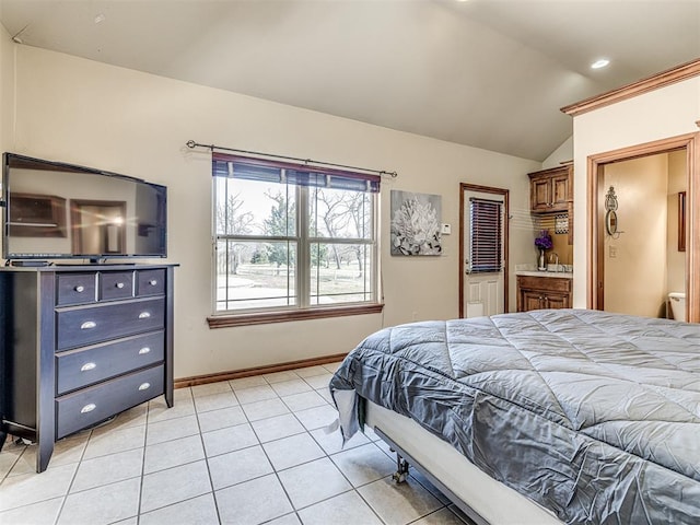 bedroom with lofted ceiling, light tile patterned floors, baseboards, and ensuite bathroom