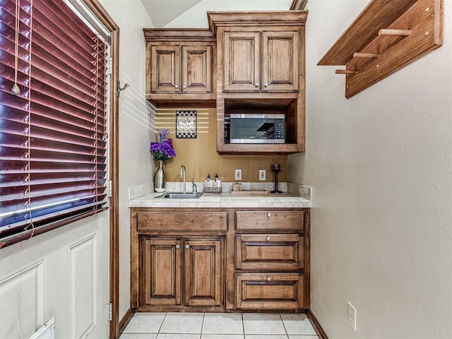 bar featuring wet bar, light tile patterned floors, baseboards, and a sink