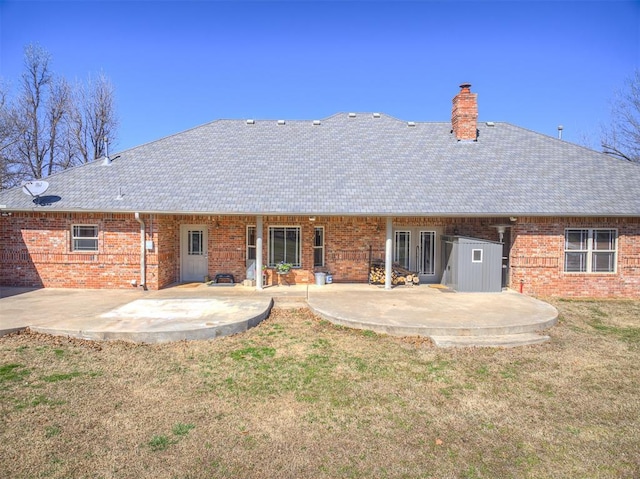 back of property with a yard, a patio area, brick siding, and a chimney