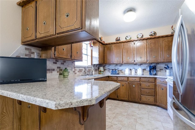 kitchen featuring a peninsula, light countertops, brown cabinets, and freestanding refrigerator