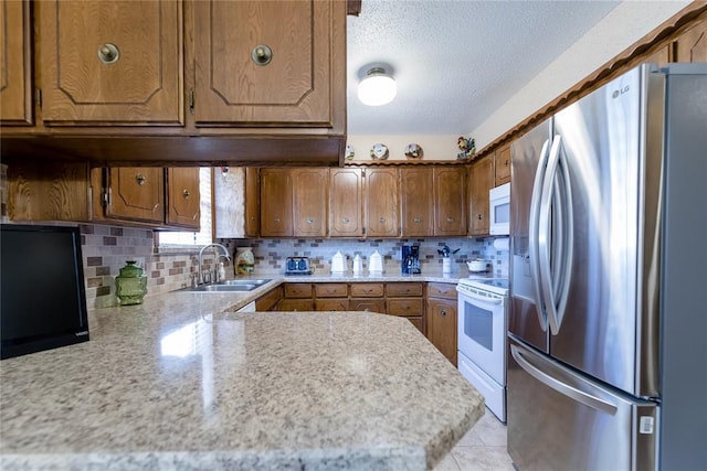 kitchen featuring white appliances, brown cabinets, a sink, light countertops, and tasteful backsplash