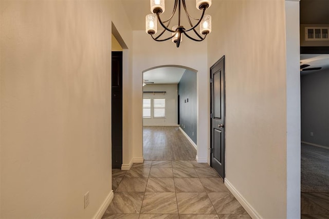 corridor featuring visible vents, arched walkways, baseboards, and a chandelier