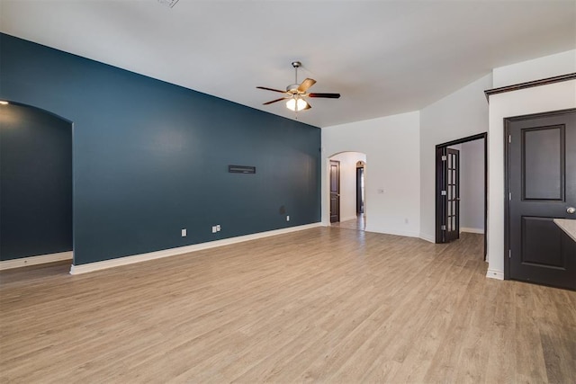 spare room with arched walkways, baseboards, light wood-type flooring, and a ceiling fan