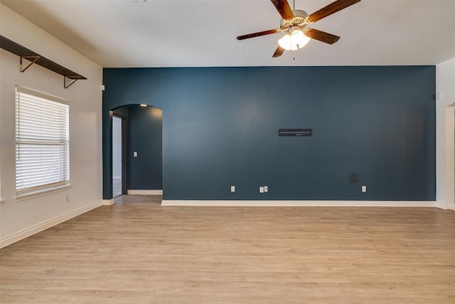 unfurnished room featuring baseboards, arched walkways, light wood-style floors, and a ceiling fan