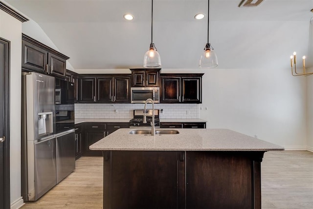 kitchen featuring light stone counters, lofted ceiling, a sink, appliances with stainless steel finishes, and light wood-type flooring