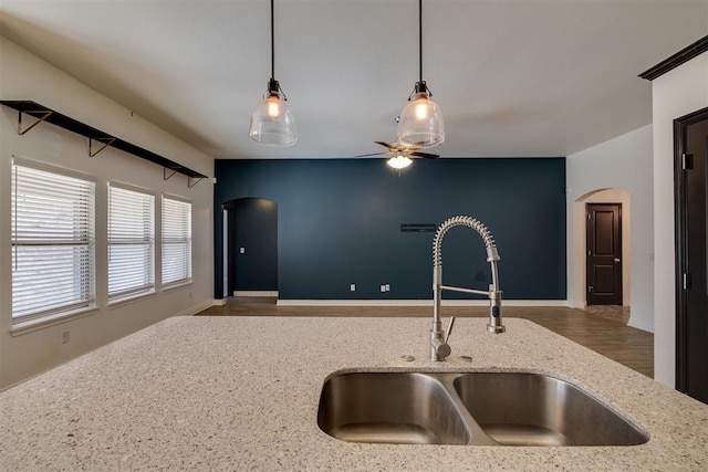 kitchen featuring arched walkways, open floor plan, light stone countertops, and a sink