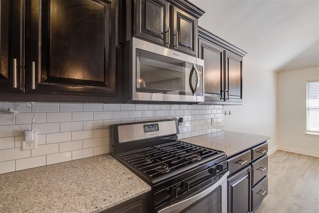 kitchen with light stone countertops, stainless steel appliances, dark brown cabinetry, tasteful backsplash, and light wood-type flooring