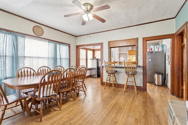 dining area featuring a textured ceiling, light wood-type flooring, ceiling fan, and ornamental molding