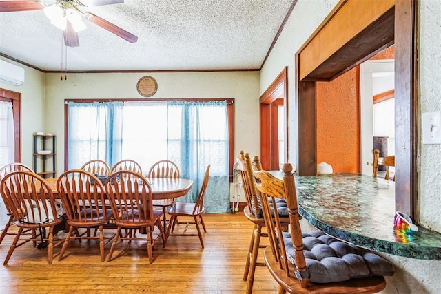 dining area with a textured ceiling, a wall unit AC, light wood-type flooring, and ornamental molding