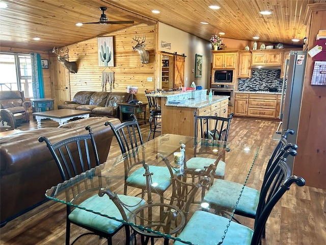 dining space with a barn door, wooden walls, wood ceiling, and wood finished floors