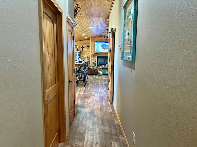 corridor with vaulted ceiling, wooden ceiling, a textured wall, and hardwood / wood-style floors