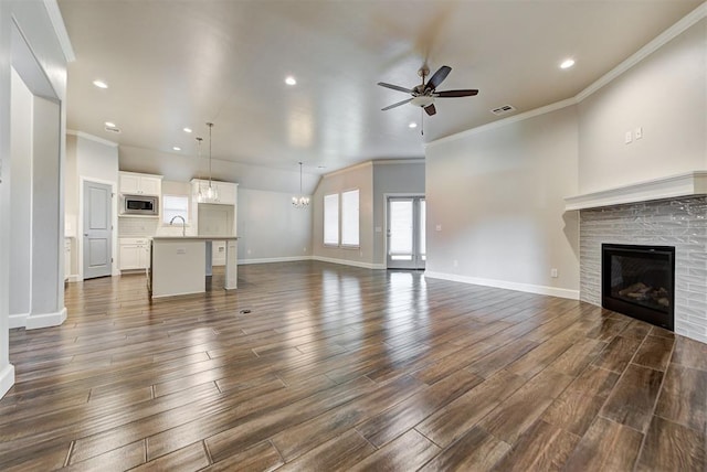 unfurnished living room featuring baseboards, dark wood finished floors, a sink, a glass covered fireplace, and ceiling fan with notable chandelier