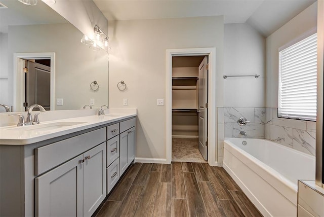 bathroom with wood tiled floor, a bath, double vanity, and a sink