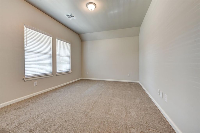 unfurnished room featuring visible vents, light colored carpet, lofted ceiling, and baseboards