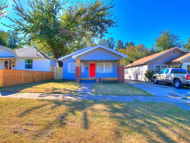 bungalow-style home with covered porch, a front lawn, and fence