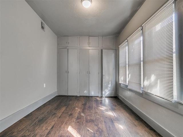 unfurnished bedroom featuring a closet, baseboards, visible vents, and dark wood finished floors