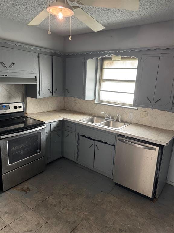 kitchen with gray cabinets, a sink, stainless steel appliances, under cabinet range hood, and backsplash