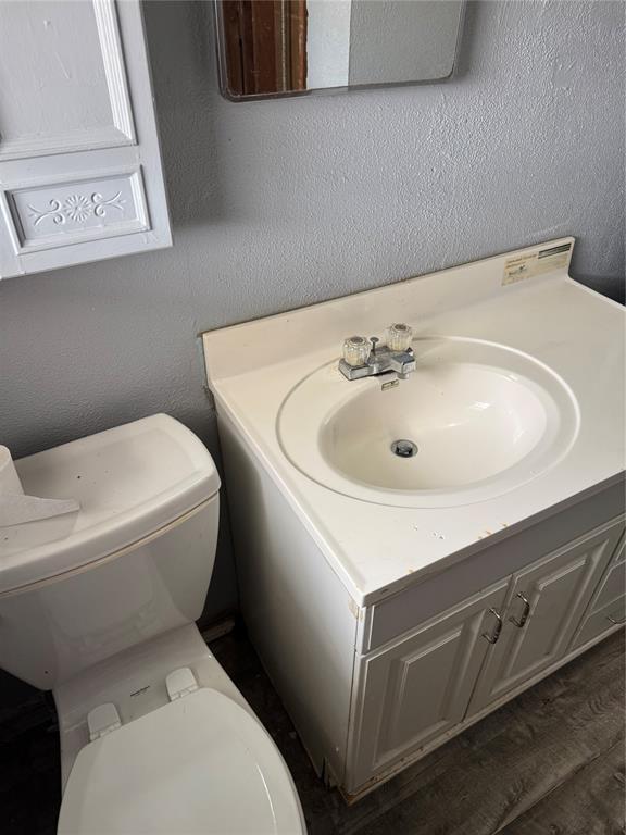 half bathroom featuring toilet, vanity, and a textured wall