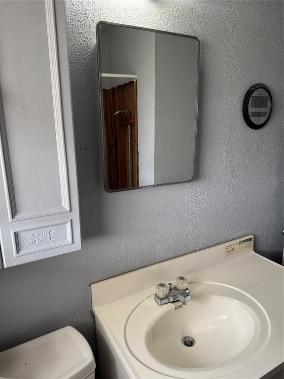 bathroom with toilet, vanity, and a textured wall