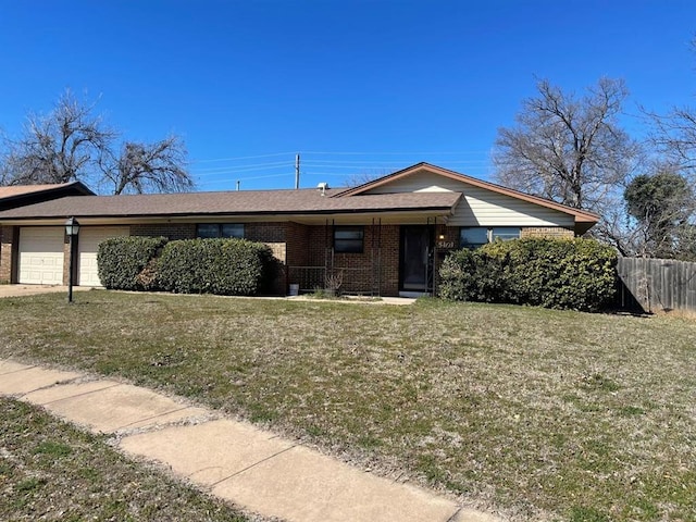 view of front facade with brick siding, an attached garage, a front yard, and fence