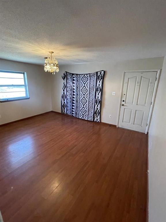 spare room with baseboards, a textured ceiling, an inviting chandelier, and wood finished floors