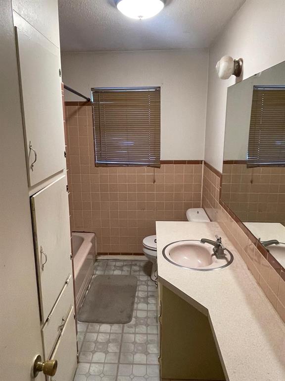 full bathroom featuring vanity, tile walls, toilet, and a textured ceiling