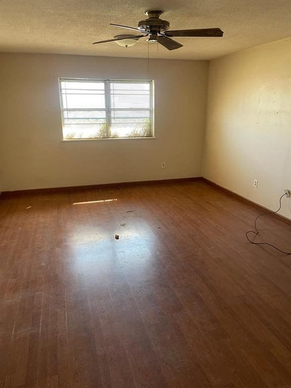 empty room with ceiling fan, a textured ceiling, baseboards, and wood finished floors