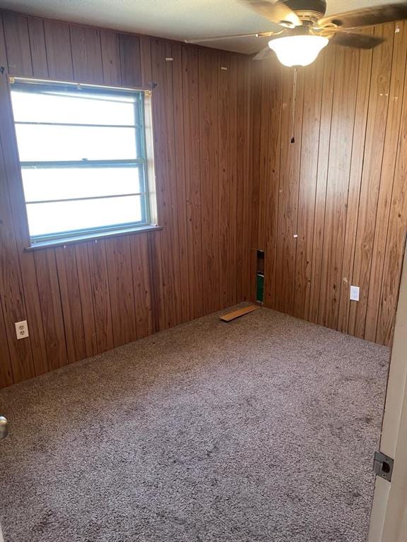 spare room featuring carpet flooring, a ceiling fan, and wood walls