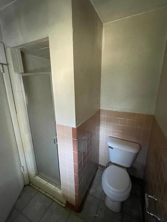 full bath featuring a wainscoted wall, a stall shower, tile patterned flooring, tile walls, and toilet