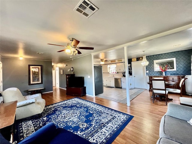 living area featuring visible vents, baseboards, a ceiling fan, and light wood finished floors