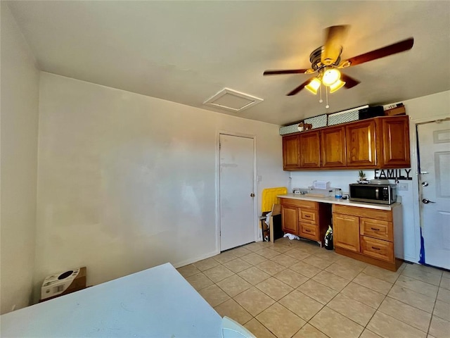 kitchen with stainless steel microwave, light tile patterned flooring, brown cabinetry, light countertops, and ceiling fan