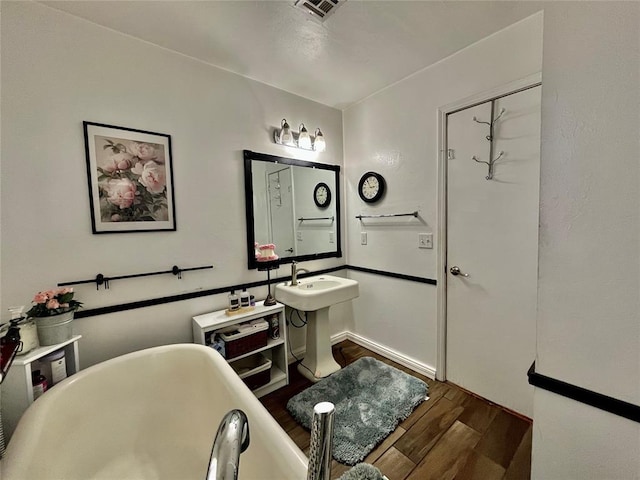 full bath featuring visible vents, a sink, wood finished floors, baseboards, and a soaking tub