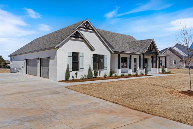 view of front facade featuring roof with shingles, covered porch, concrete driveway, central air condition unit, and brick siding