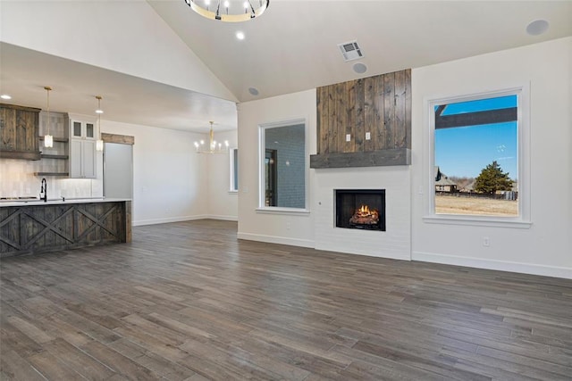 unfurnished living room featuring visible vents, high vaulted ceiling, dark wood finished floors, a notable chandelier, and a large fireplace