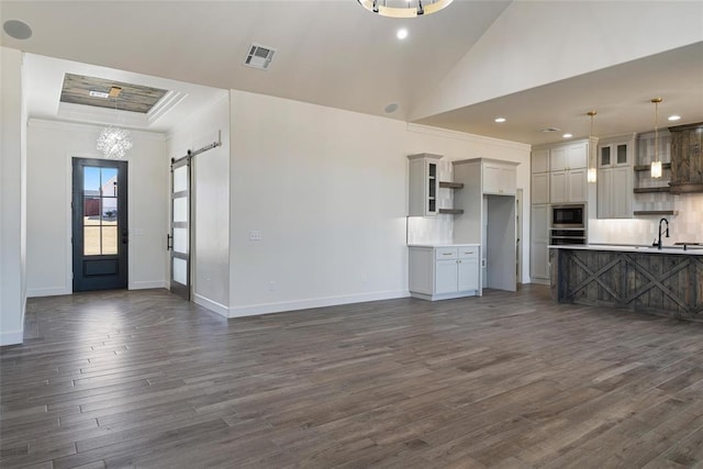 unfurnished living room featuring visible vents, baseboards, dark wood finished floors, a barn door, and a raised ceiling