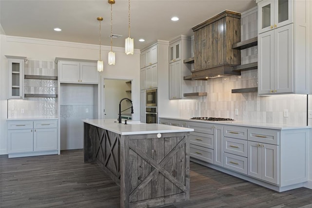 kitchen featuring a center island with sink, open shelves, a sink, light countertops, and stainless steel gas stovetop