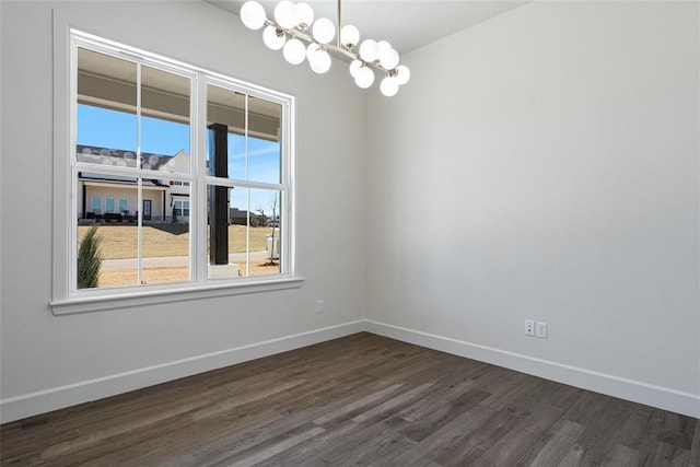 spare room with dark wood finished floors, a notable chandelier, and baseboards