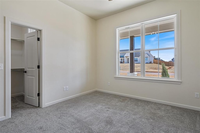 unfurnished bedroom with a closet, carpet flooring, a walk in closet, and baseboards