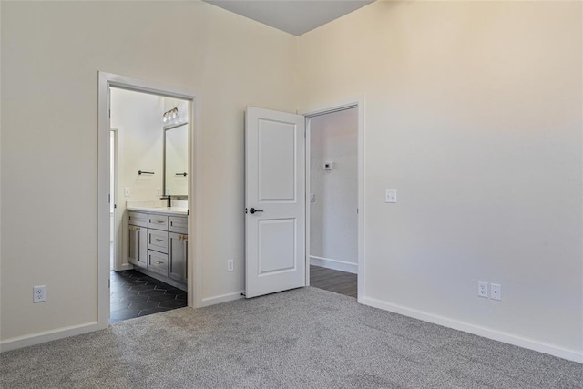 unfurnished bedroom featuring dark carpet, connected bathroom, baseboards, and a sink