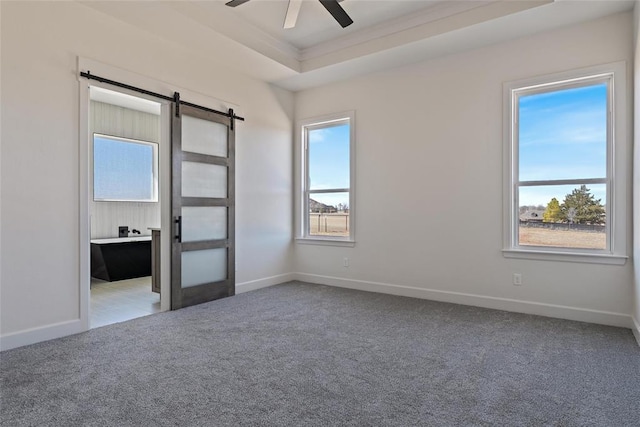 empty room featuring a ceiling fan, carpet, baseboards, a barn door, and a raised ceiling