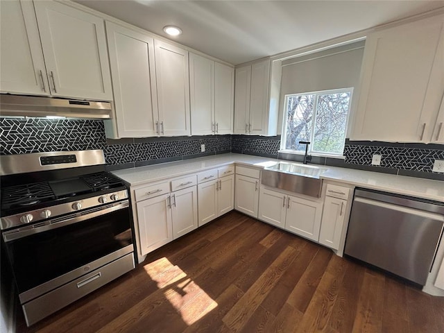 kitchen featuring a sink, stainless steel appliances, light countertops, dark wood-type flooring, and under cabinet range hood