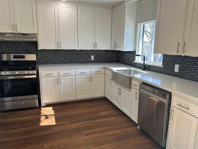 kitchen featuring under cabinet range hood, appliances with stainless steel finishes, dark wood-style floors, white cabinetry, and a sink