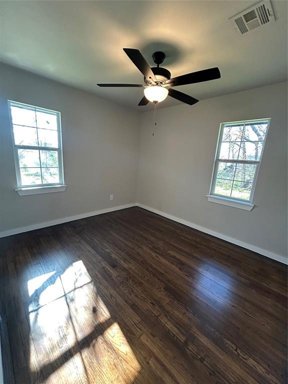 empty room featuring dark wood finished floors, baseboards, visible vents, and a wealth of natural light