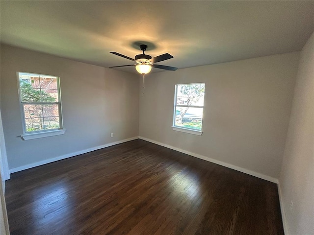 empty room featuring a wealth of natural light, dark wood-type flooring, and baseboards